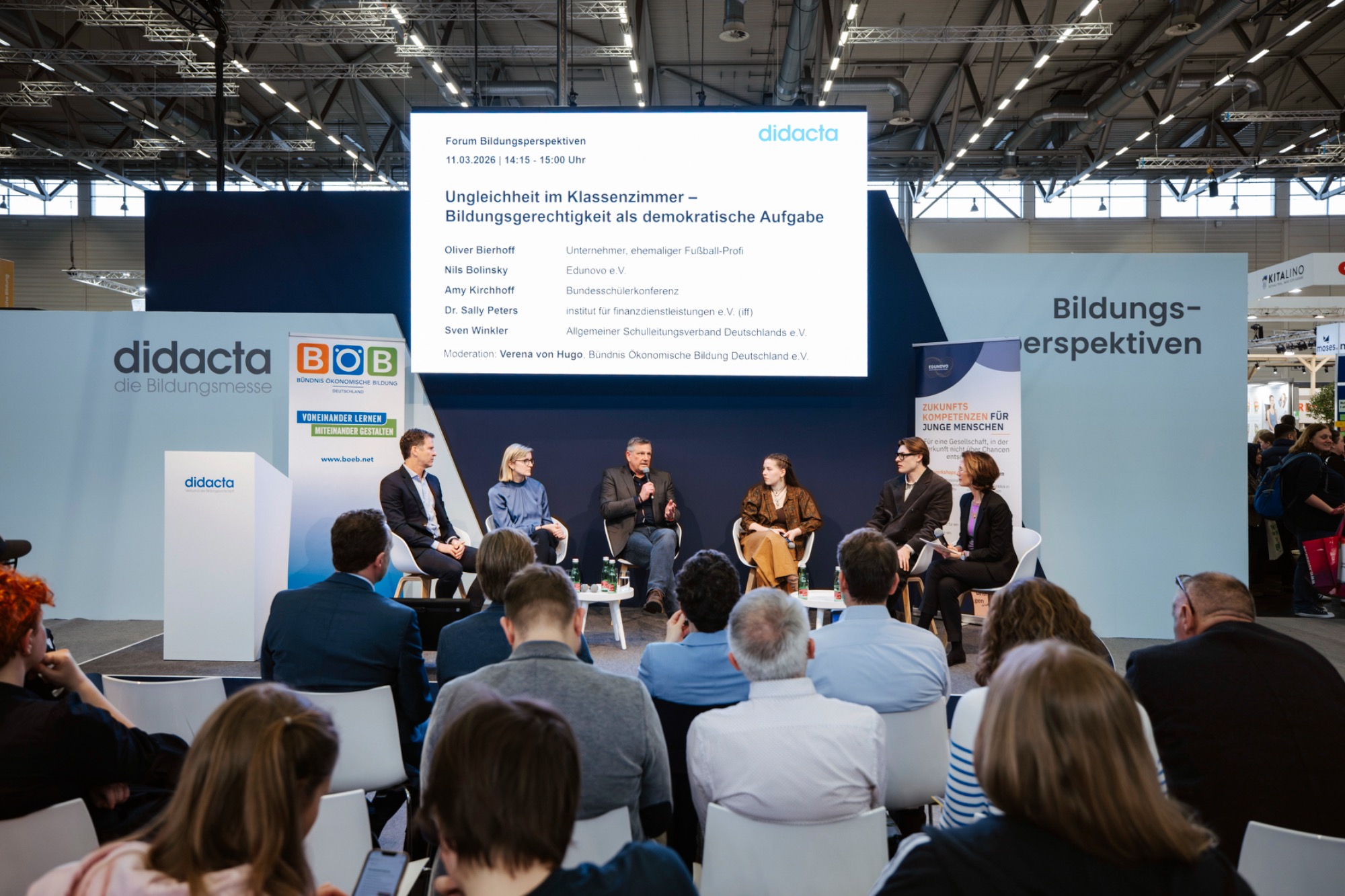 Didacta 2026 Podiumsdiskussion mit mehreren Speakern auf einer Veranstaltung. Hintergründe in Grau und Blau.