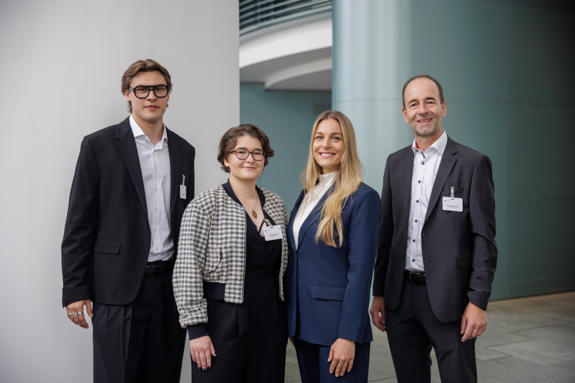 Unsere startsocial Coaches Lisa und Konrad Vier Personen in formeller Kleidung stehen in einem modernen Innenraum.